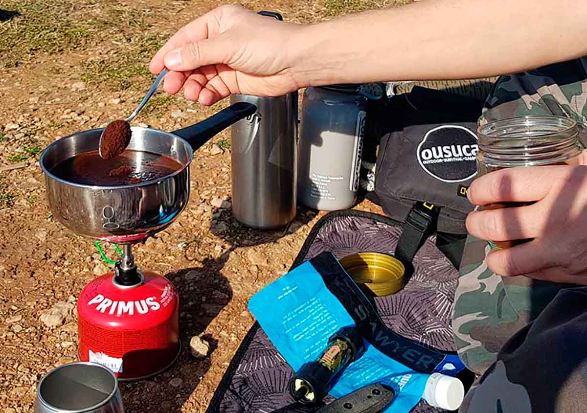 Zubereitung von Campingkaffee in Topf auf einem Gaskocher.