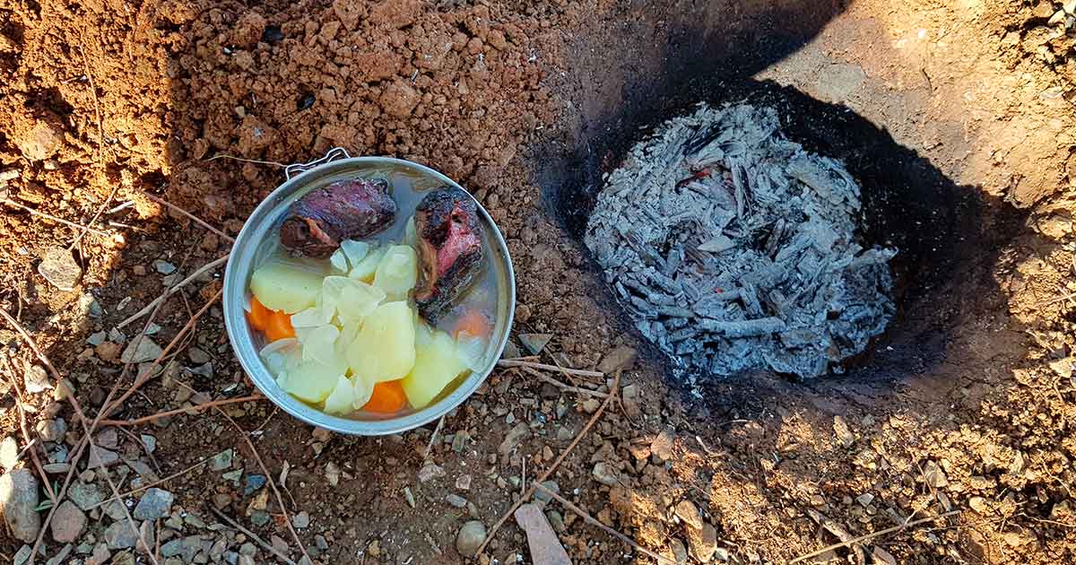 Essen kochen über Feuer: Gemüseeintopf mit gegrilltem Schweinefleisch vom Dakota Fire Hole